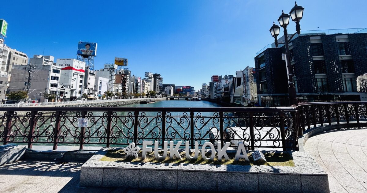 福岡中州の街並み　橋のたもとに「FUKUOKA」と書いた看板が見えて、その奥に中州が広がっている
