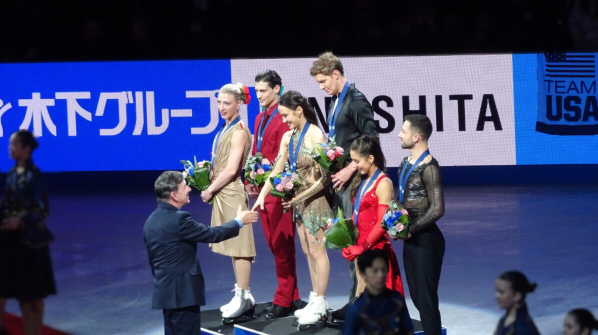 アイスダンス表彰式でメダリストたちに花束が贈呈されている時の表彰台メンバー全景　マディソン・チョック選手が花束贈呈者と握手をしている
