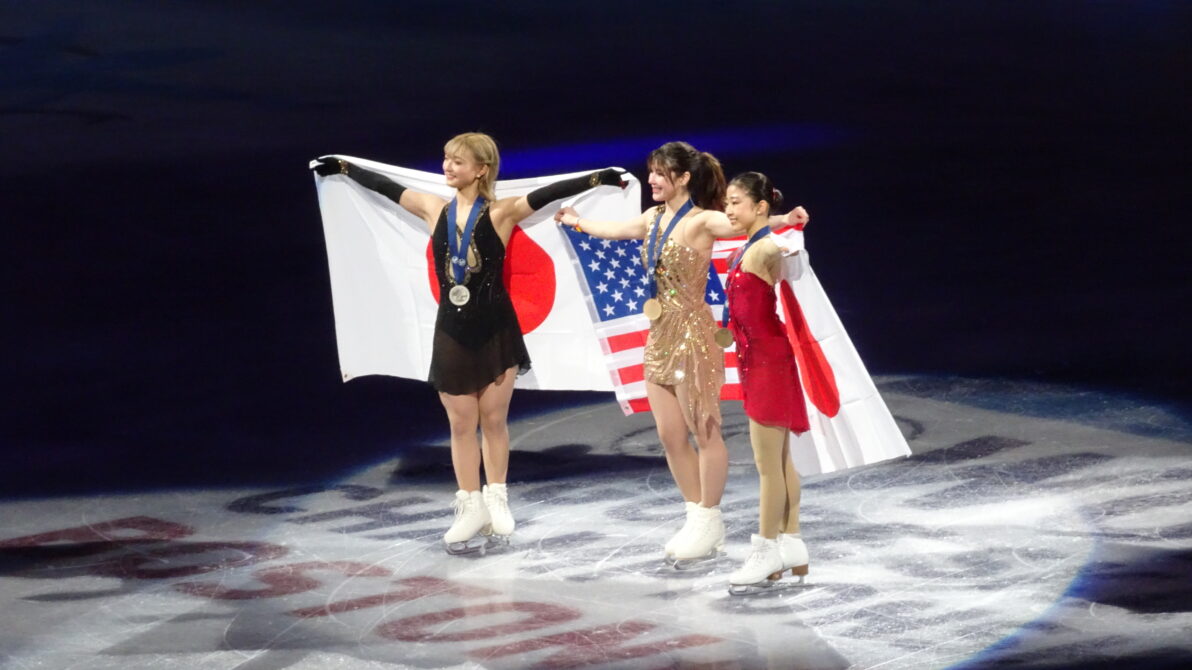 国旗を背にリンク上で笑顔で記念撮影する女子シングルメダリスト達３名