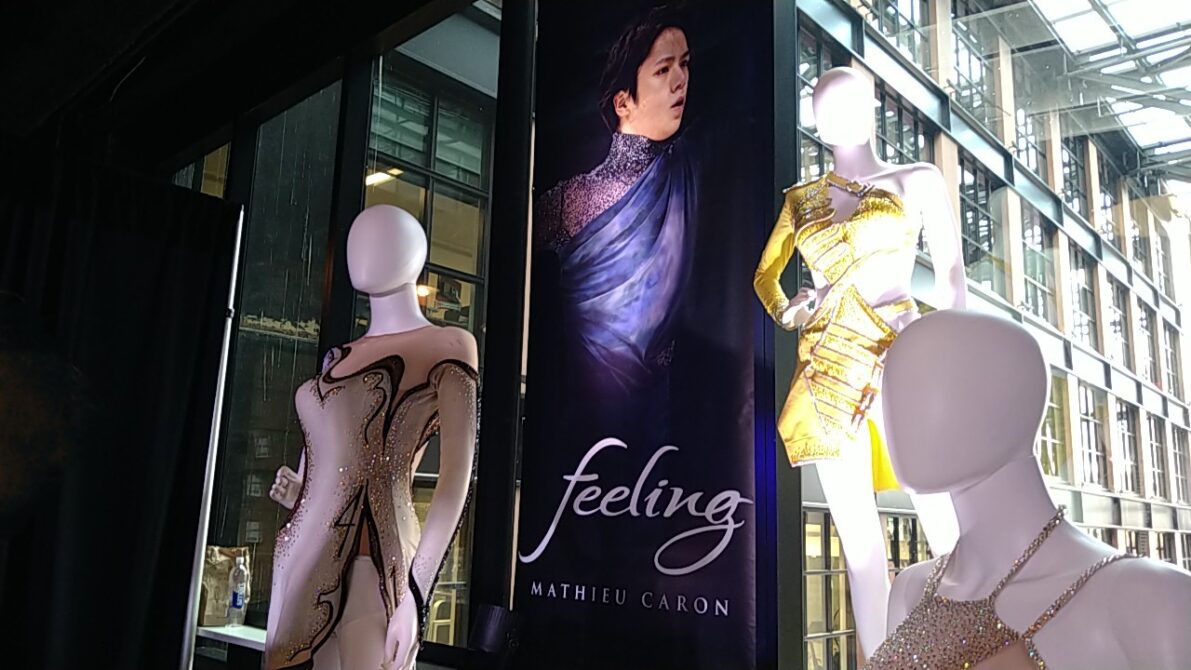 窓に宇野昌磨さんのタペストリーがかかっていて、手前に女性のフィギュアスケート衣装を着たマネキン三体が並んでいる