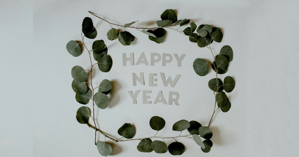 白地にHAPPY NEW YEARの文字が掛かれ、緑の葉がついた木の枝を文字の周囲を囲んでいる写真