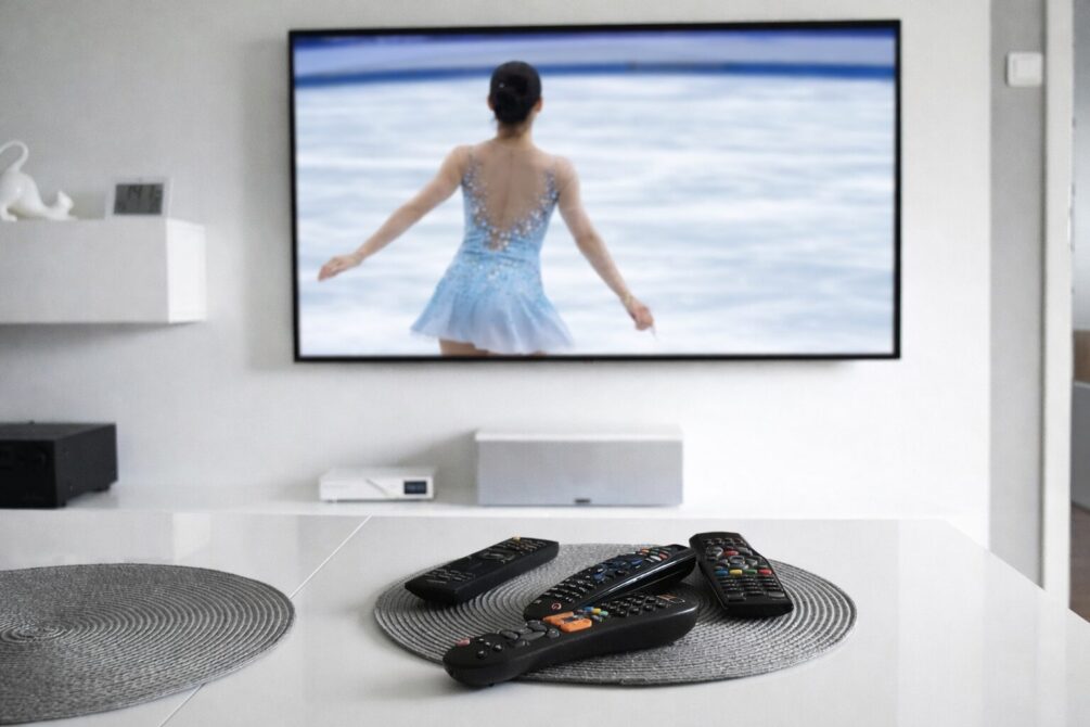 フィギュアスケートの女性選手が映っているテレビ画面の前にリモコンが並んでいるリビングルーム