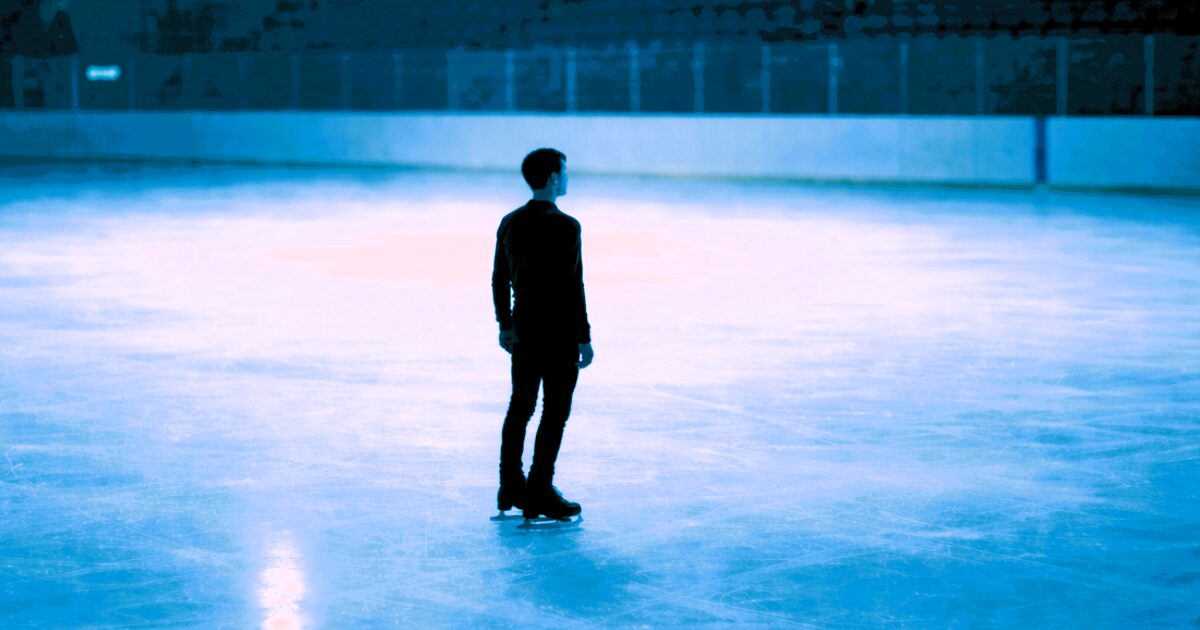 暗いリンクで一人前を向いてたたずむ男性スケーターのシルエット画像