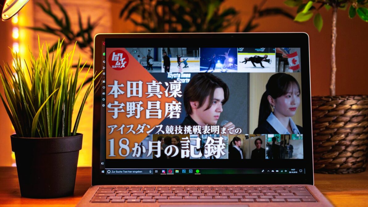 暖色系のライトがつくデスク上のPC画面に本田真凜・宇野昌磨の密着動画のサムネイルが映っている写真