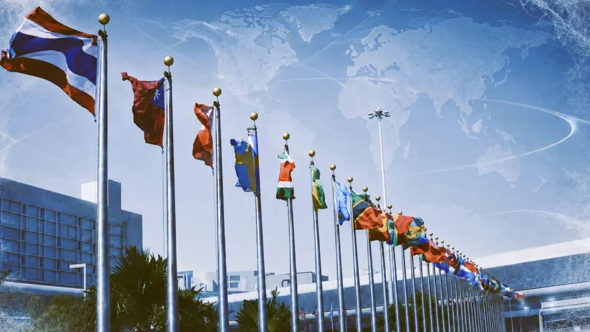 空の下にたなびく世界各国の国旗、空には世界地図とスケートのトレースらしき雲がかかっている