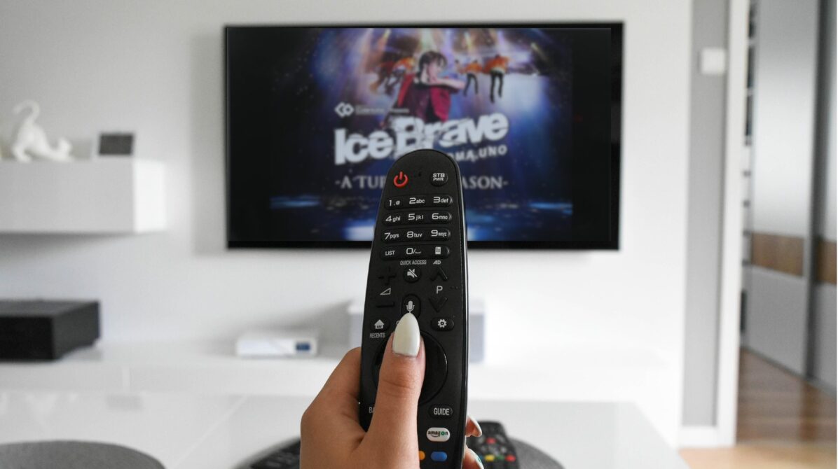 白を基調としたリビングのテレビをリモコン操作する手元、テレビにはIce Brave-A TURNING SEASON-の宣伝ビジュアルが映っている